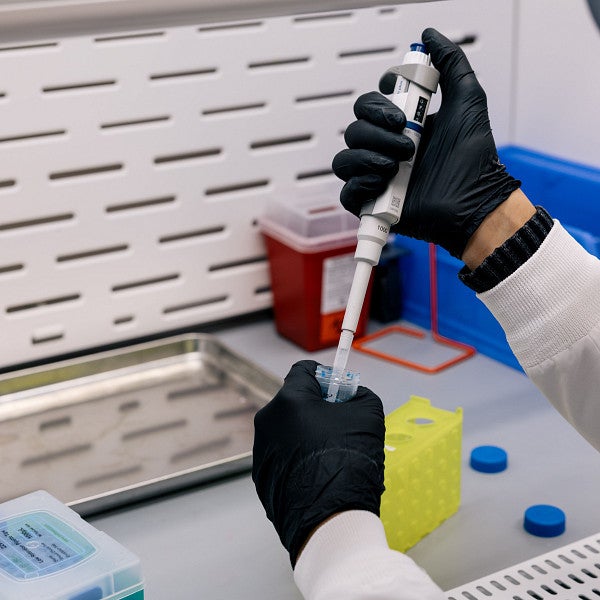 Gloved hands conducting STEM research with a pipette and text tube
